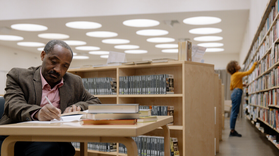 Pessoas em uma biblioteca estudando e escolhendo livros de teoria literária