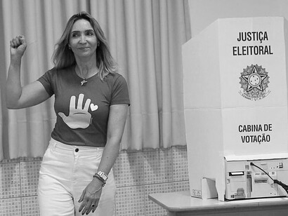Diante da urna eletrônica, uma eleitora ergue o punho em um gesto de afirmação política. A cena remete à ideia de que o direito de escolher também é uma forma de participação e posicionamento na vida pública