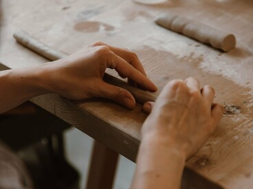 Uma pessoa trabalha a massa com as mãos sobre uma mesa, concentrando-se nos movimentos de modelagem. Assim como na cerâmica artesanal, a repetição dos gestos e o controle da pressão são fundamentais para alcançar a forma desejada