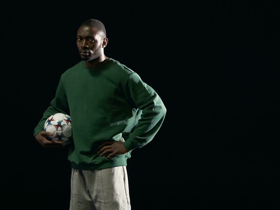 A man in a green sweater holding a soccer ball