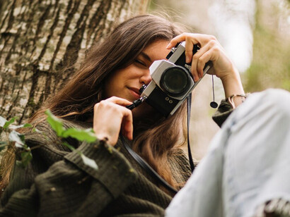 A young woman sits on a tree in nature, holding a camera, embodying the essence of stillness and mindfulness in quiet moments