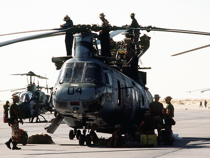 Marines rest beside a CH-46 Sea Knight helicopter as fellow service members inspect the rotors before takeoff during Operation Desert Storm