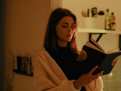A woman wearing a white sweater is quietly reading a book at home