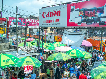 Entre étals et parasols verts, la vie quotidienne à Lagos continue, illustrant comment la population poursuit ses activités malgré l’ombre des conflits et des interventions étrangères