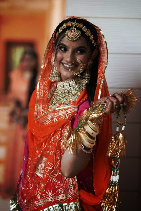 A traditional Kumaoni wedding: a radiant bride adorned in vibrant red attire and golden bracelets, celebrating love and culture