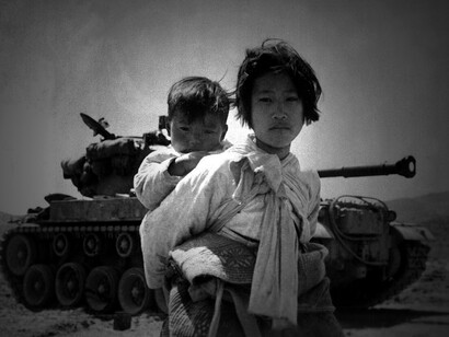 With her brother on her back a war weary Korean girl tiredly trudges by a stalled M-46 tank, at Haengju, Korea