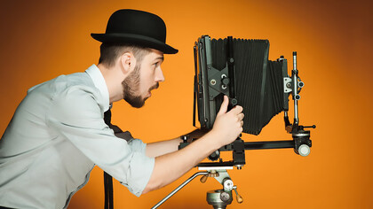 A young man with a retro camera is captured alongside film projector, movie screen, film camera, and film editing equipment, embodying the essence of cinematic artistry and production