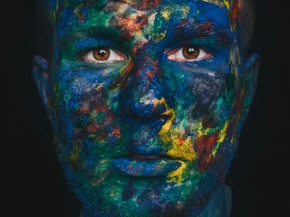 A man with face paint all over is seeing with his natural brown eyes without willing to go ahead with a Keratopigmentation surgery