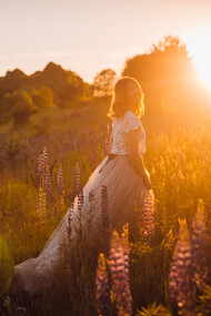 A woman in a bright dress walks across a field in the glow of sunset
