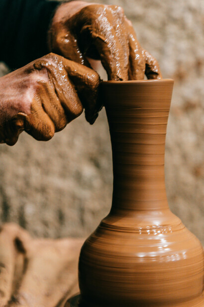 Man forming a clay vase in a bright artist studio with natural light, surrounded by craft supplies on the desk