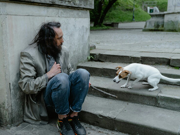 In the USA, a homeless man in blue denim jeans sits beside a white short coat left on the ground