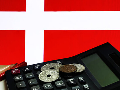 Stack of Denmark coins with red and wooden pen on white background with calculator on Danish nation flag background