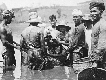 Indigenous fishers showing each other their catch while wearing traditional clothing