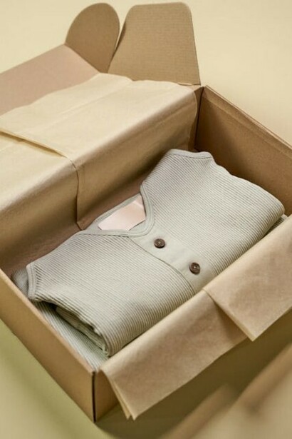 An individual packaging eco-conscious clothing in a cardboard box, highlighting the use of sustainable, plant-based materials