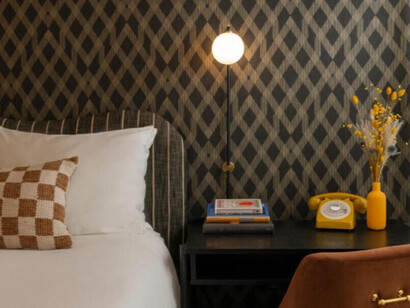 The bed with crisp white bedding and pillows. The headboard is upholstered in a dark brown fabric with a rounded shape, adding a gentle contrast to the wall paper