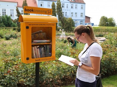 Una lectora leyendo un libro frente a una urna diseñada para el bookcrossing