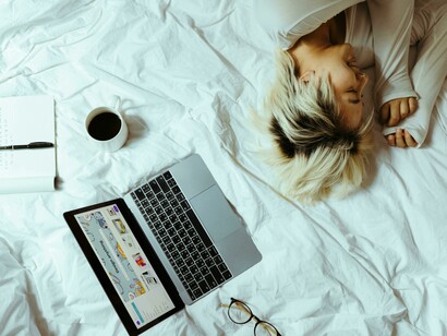Student sleeping on a bed near a laptop and a cup of coffee, studying