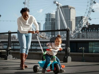 In the park, a woman gently guides her child on a tricycle