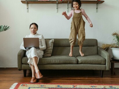 Mujer sentada en un sillón y niña saltando a su lado