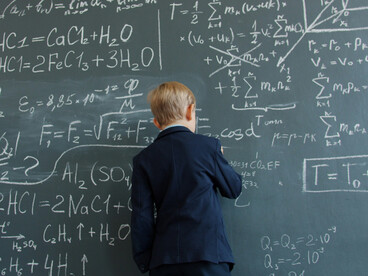 Un garçon écrivant des formules complexes sur un tableau, représentant le rôle des puissances distribuées dans les processus cognitifs et la manière dont des systèmes de coordination entre le cerveau et l’environnement façonnent les actions cognitives