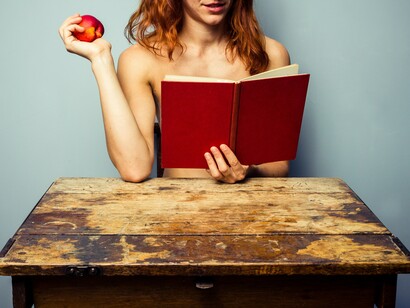 Una mujer comiendo fruta y leyendo desnuda
