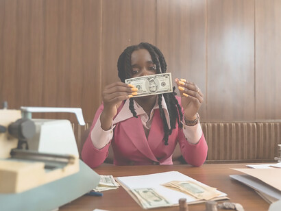 A woman in pink blazer holding paper money against face