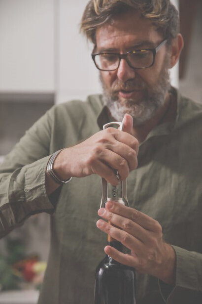 The man deftly extracts the wine cap from the bottle