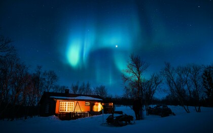 A brown cottage beneath a glowing aurora borealis