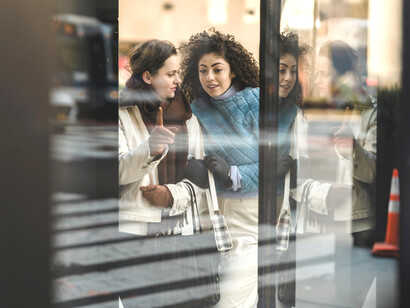 Through the shop window, cheerful and diverse women with shopping bags enjoy a day of luxury shopping