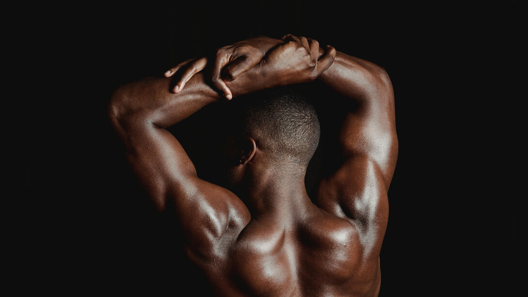 Back view of a shirtless man posing to showcase his muscles and physical fitness