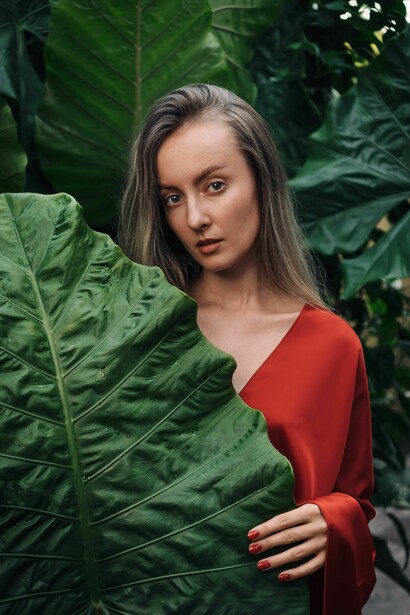 Mulher parcialmente escondida por uma grande folha tropical. A imagem sugere aquilo que permanece oculto e precisa ser reconhecido; uma ideia próxima do encontro com a própria sombra mencionado no texto