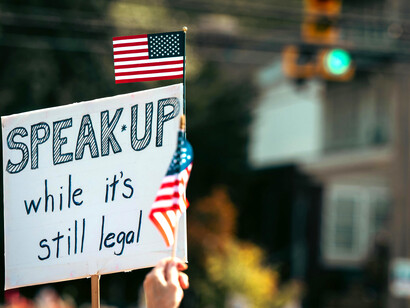 Protest sign displayed alongside the American flag during a public rall, USA