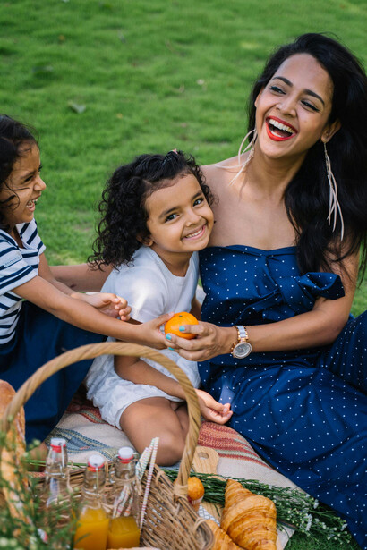 An Indian woman in a blue dress sits on a picnic mat with two girls
