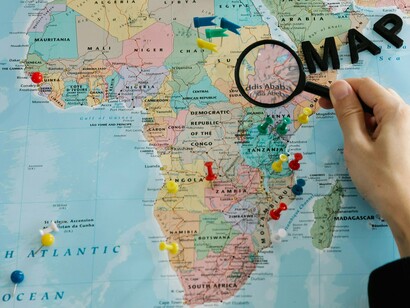 Africa marked with colorful pushpins and a hand holding a magnifying glass, symbolizing the strategic focus on the continent's resources and the internal and external forces at play in its political landscape