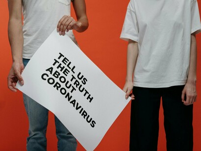 A pair standing together holding a placard demanding the truth about COVID-19, representing public distrust shaped by fear and conflicting narratives