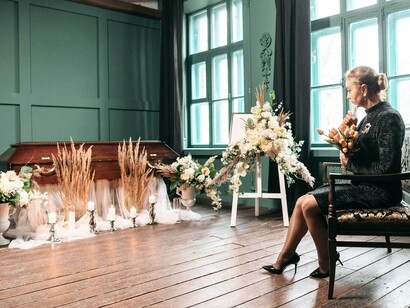 A woman seated before a coffin surrounded by candles, reflecting the isolation and grief during the epidemic years
