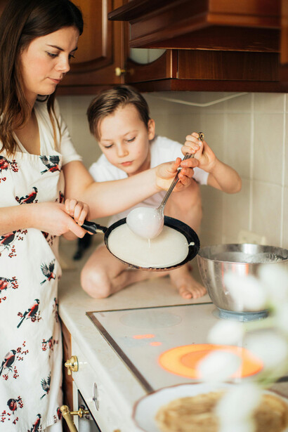 A mother and child prepare crepes together in the kitchen, reflecting everyday family life