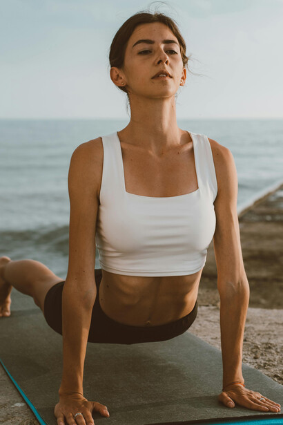 An adult woman sits in meditation on a yoga mat by the ocean, finding peace and balance in the calm outdoor atmosphere