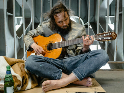 Bearded man sitting on the ground, experiencing homelessness and poverty