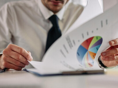 A person analyzing business reports, taking notes in the office, and studying stock market trends, options trading, and financial graphs to refine trading strategies