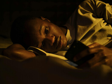 An anxious person scrolling through their phone late at night, unable to disconnect