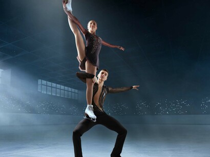 A pair of figure skaters glide across an empty ice arena, highlighted by a soft spotlight in the cold atmosphere