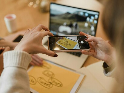 Uma criadora de conteúdo registra imagens com o celular durante uma reunião descontraída. No digital, cada detalhe pode se transformar em estratégia, conexão e presença constante para uma marca