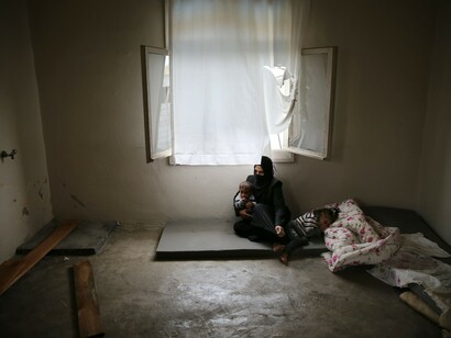Una refugiada siria con sus dos hijos en una habitación sucia y desordenada