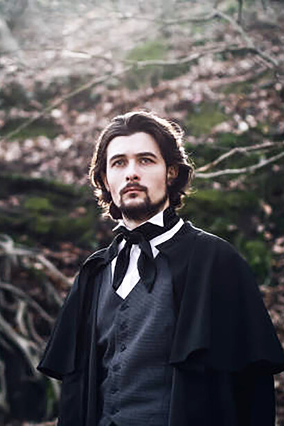 A young man dressed in a Victorian-era suit stands confidently