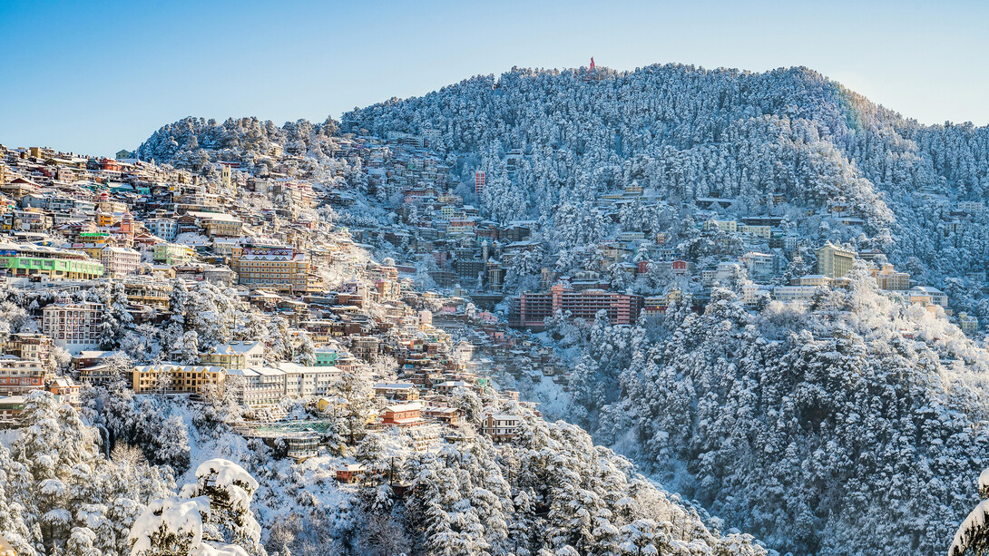 A stunning snowy mountain view from Shimla, Himachal Pradesh, India, with pristine white peaks rising majestically against a clear blue sky, creating a serene and magical atmosphere