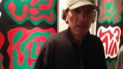 Giuliano Cotellessa con alle spalle dei quadri della propria mostra