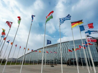 As bandeiras dos países-membros tremulam em frente à sede da OTAN, uma das principais instituições de segurança coletiva do mundo ocidental. O artigo analisa como a estabilidade dessa arquitetura internacional vem sendo questionada diante das novas tensões geopolíticas. Sede oficial da OTAN em Boulevard Leopold III, 1110 Bruxelas, Bélgica