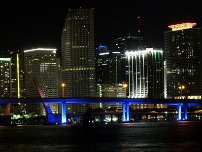 The city’s glowing bridges and towering buildings reflect its history of aggressive marketing and rapid expansion tied to tourism, real estate, and racialized consumer culture