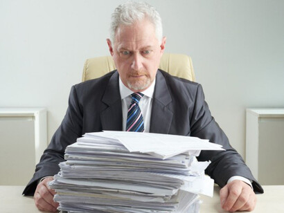Senior official surrounded by stacks of paperwork, reflecting bureaucratic overload